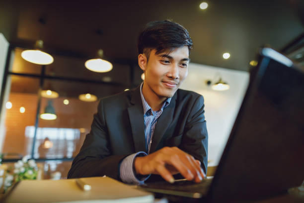 Smiling Asian businessman in suit working with laptop